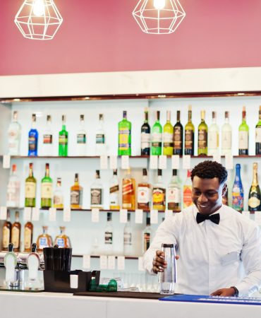 African american bartender at bar with shaker. Alcoholic beverage preparation.